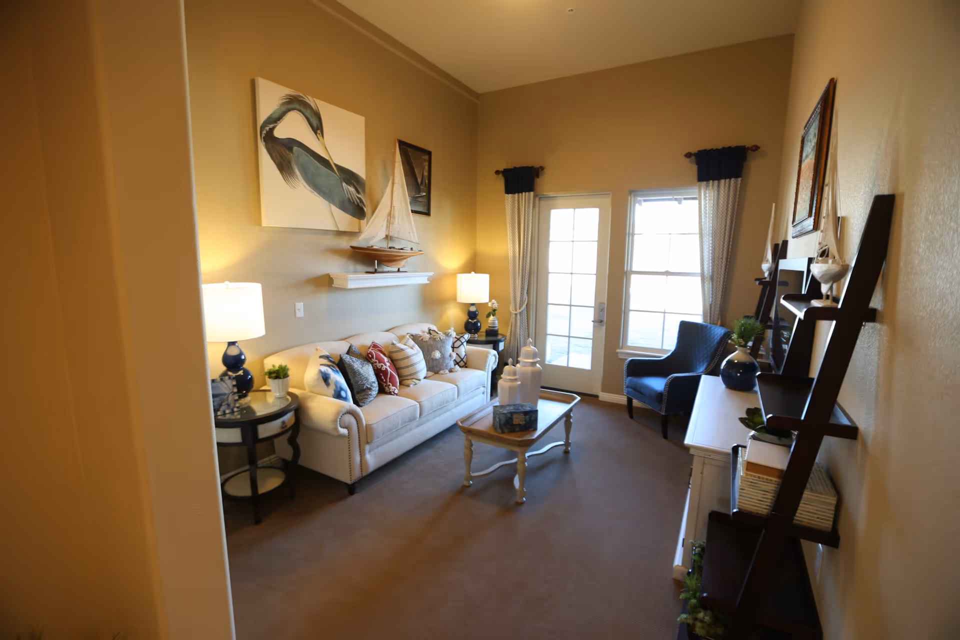 Well-lit living room with a sofa, armchair, coffee table, decorative sailboat and wall art, and French doors letting in light.