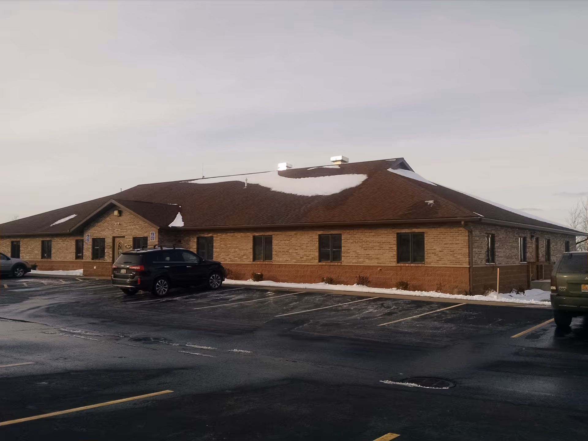 Single-story brick senior living facility exterior with a snow-dusted roof and surrounding parking lot.