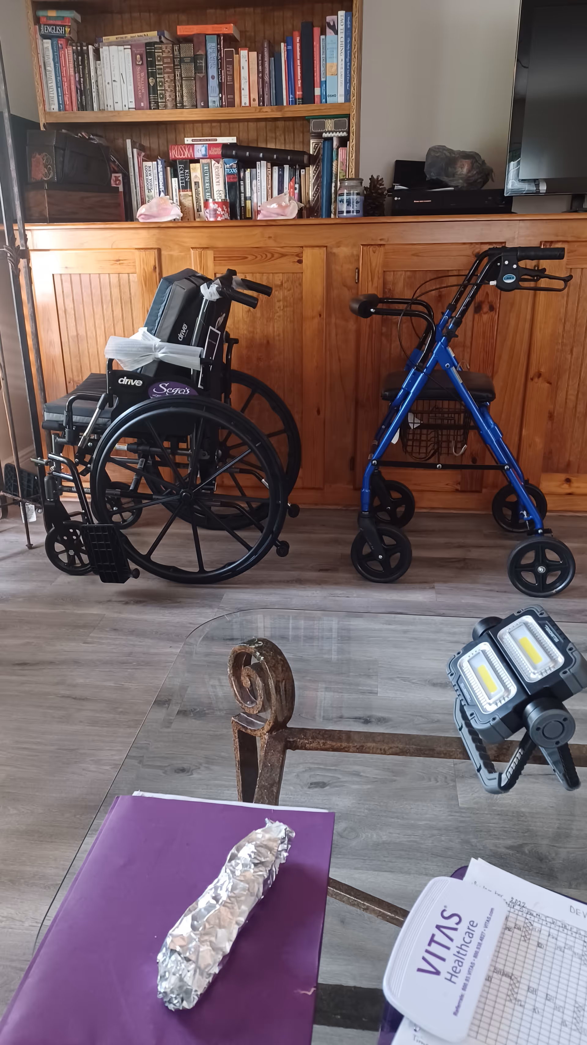 A wooden bookcase behind a wheelchair and blue walker in a cozy living room.