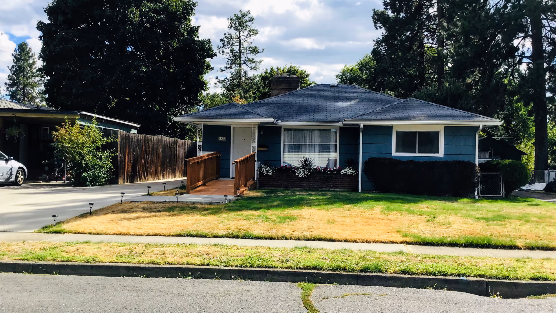Single-story blue house exterior with ramp entrance and small front lawn.
