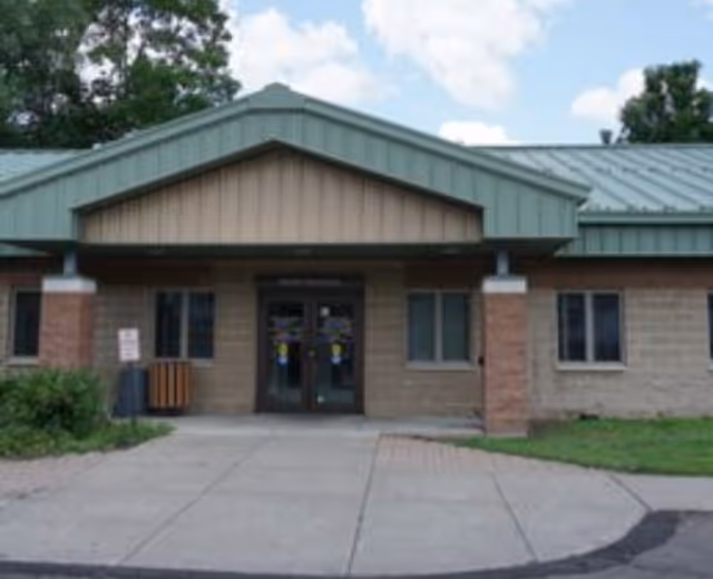 Front entrance of a brick building with a green metal roof and glass doors.