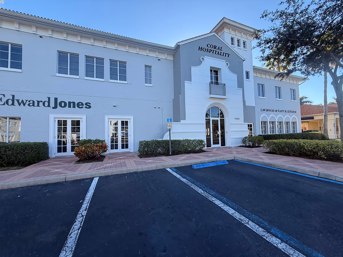 Exterior of a white commercial building with arched entry and parking lot.