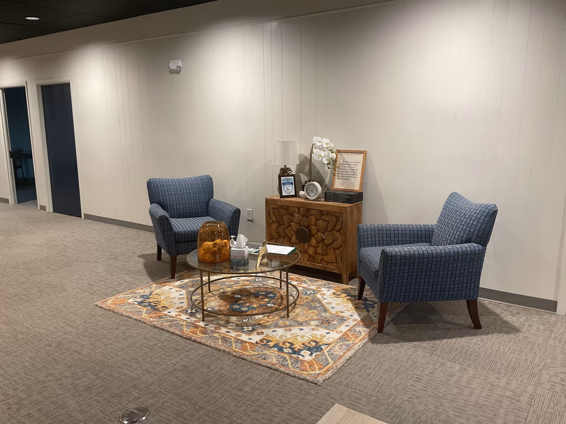 Two blue armchairs around a glass coffee table in a lounge with a decorative rug.