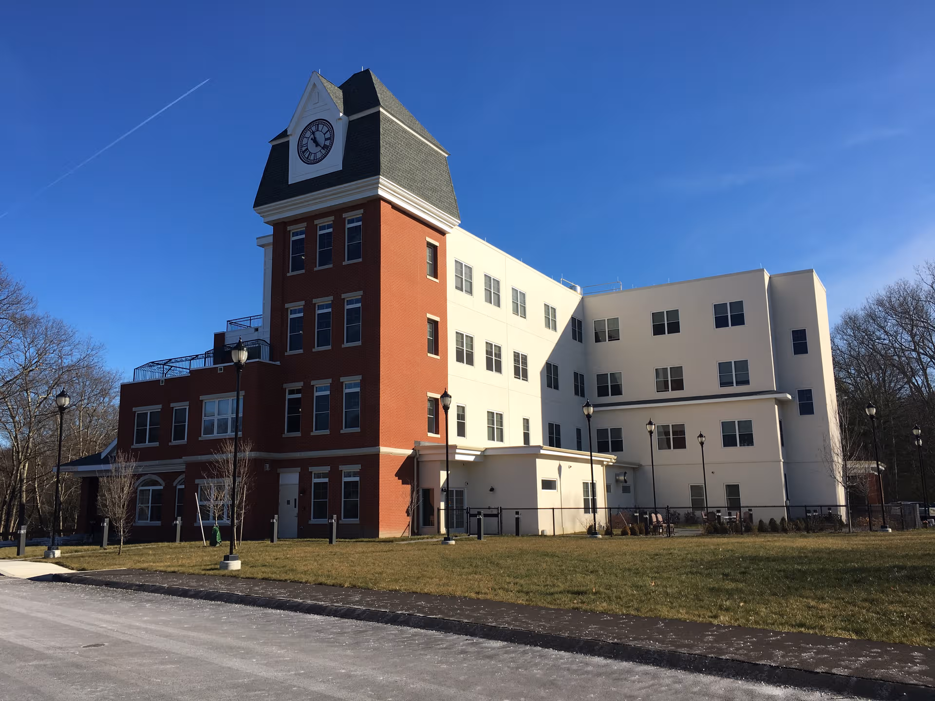 A multi-story red brick and white building exterior with a clock tower and lawn.