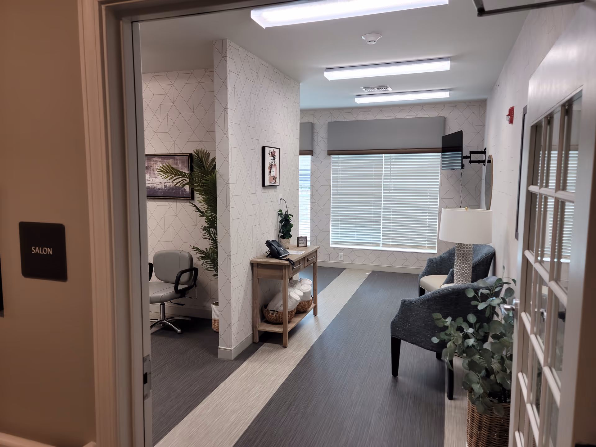 Lounge area with seating, desk, plants, and salon door in Charter Senior Living of White House.
