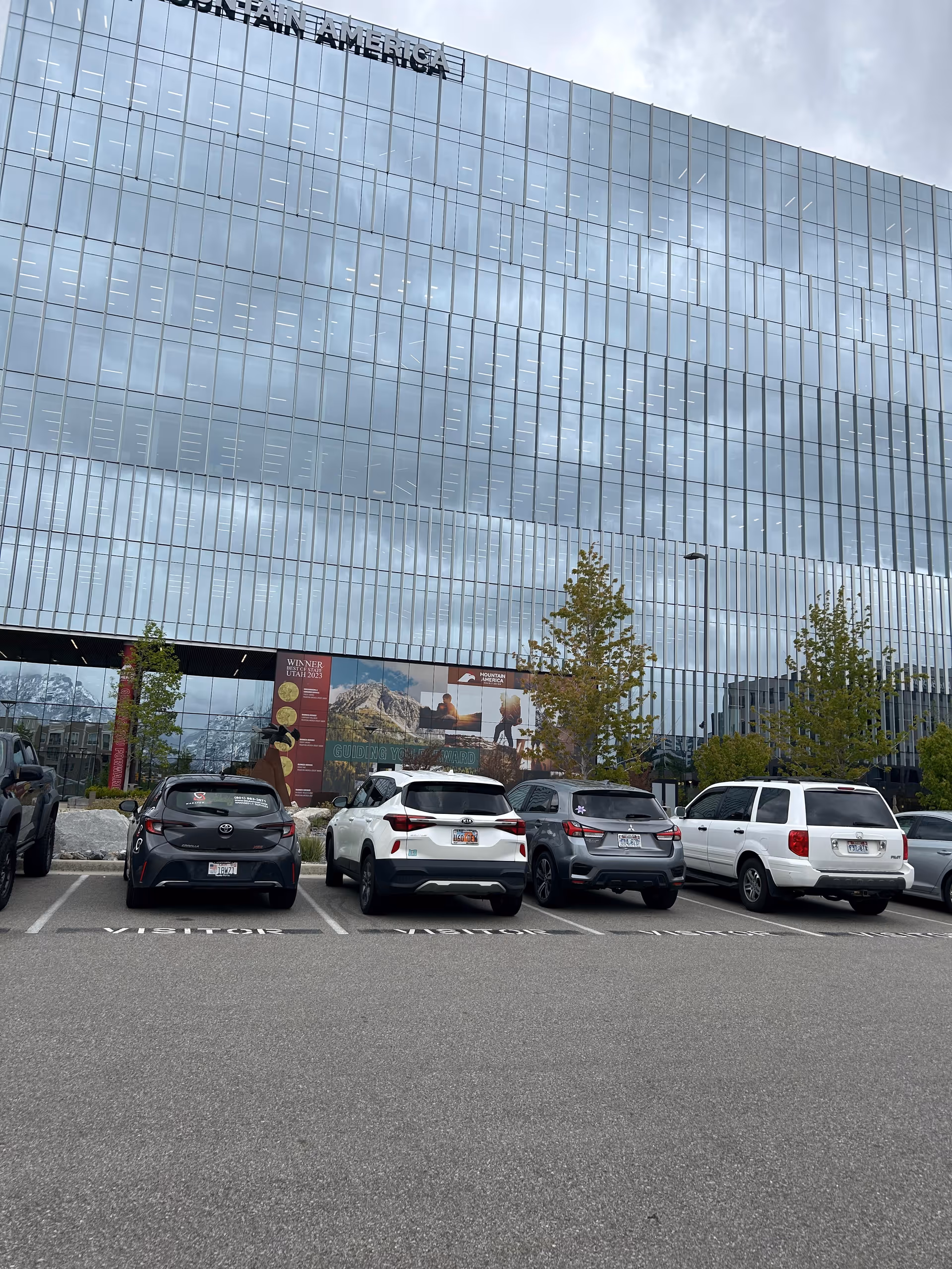 A modern glass-front building with several parked cars in front.