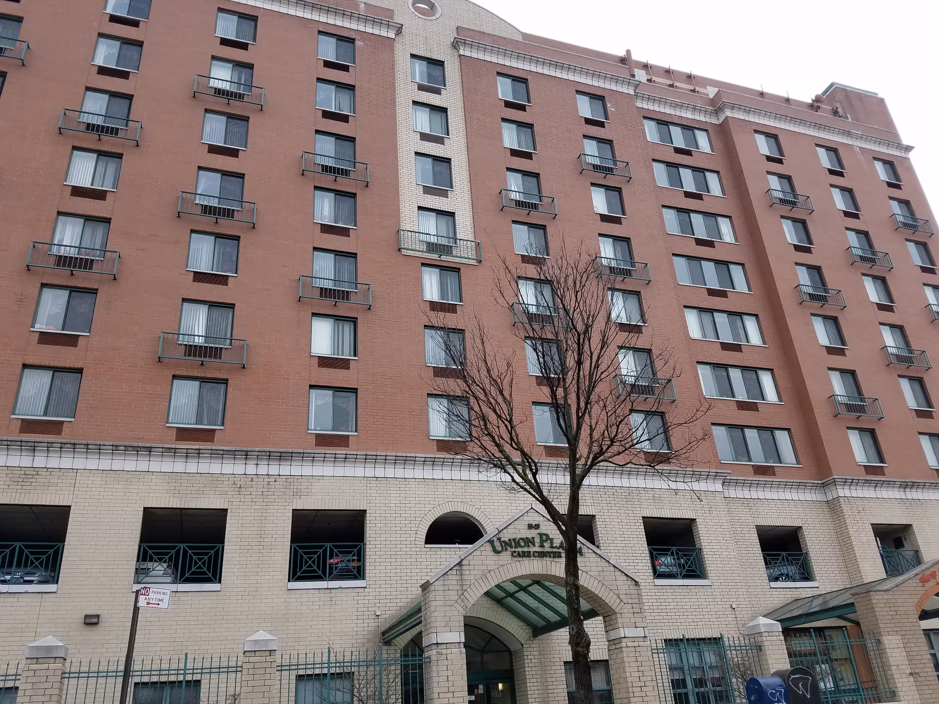 A multi-story brick Union Plaza Care Center exterior with arched entrance and a bare tree.
