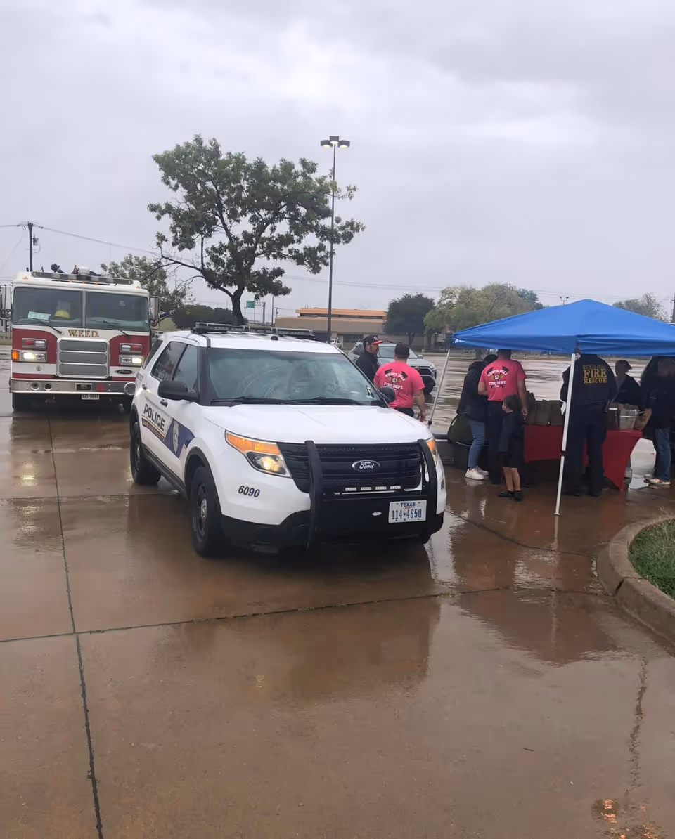Police SUV and fire truck outdoors beside a blue canopy in a parking lot.