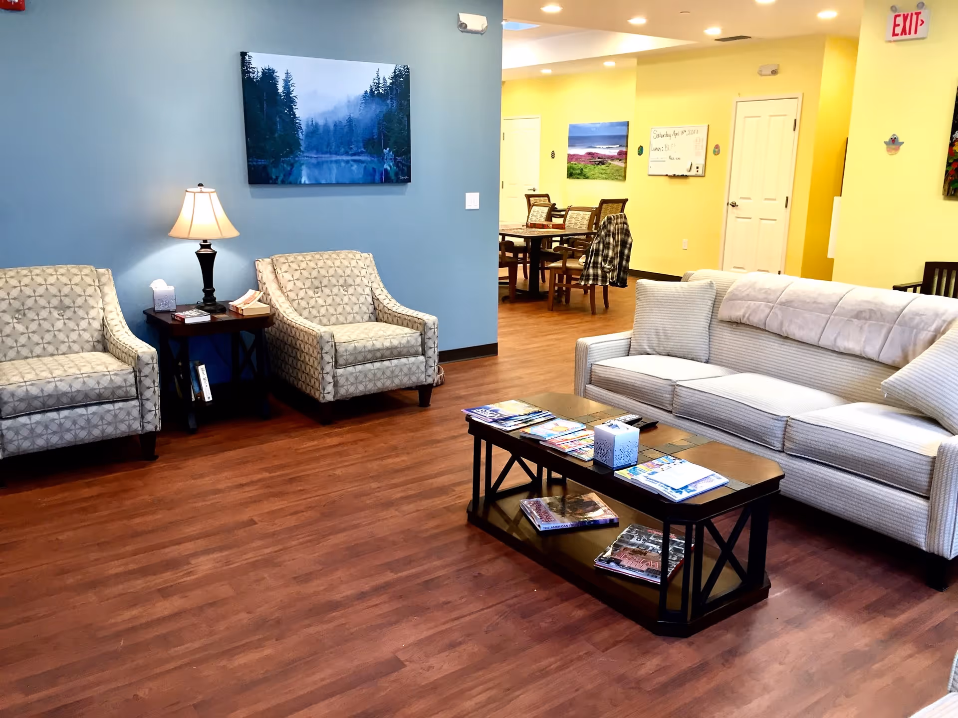 A modern senior living lounge with blue and yellow walls, seating, and a coffee table.