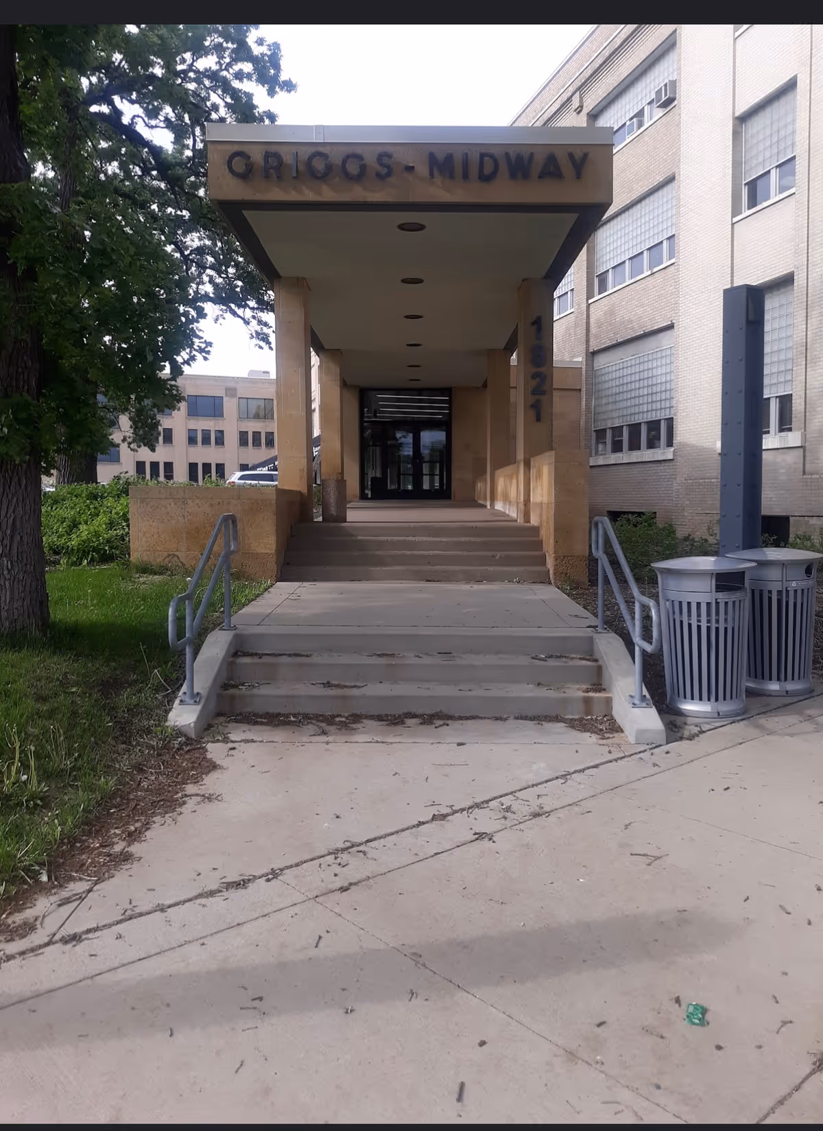Exterior view of a building entrance with steps, canopy, and rails.