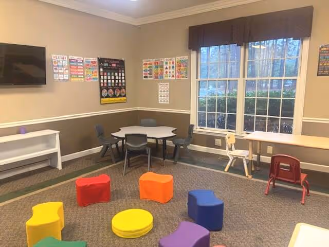 Child-friendly ABA therapy room with colorful cushions, small tables, posters, and a large window.