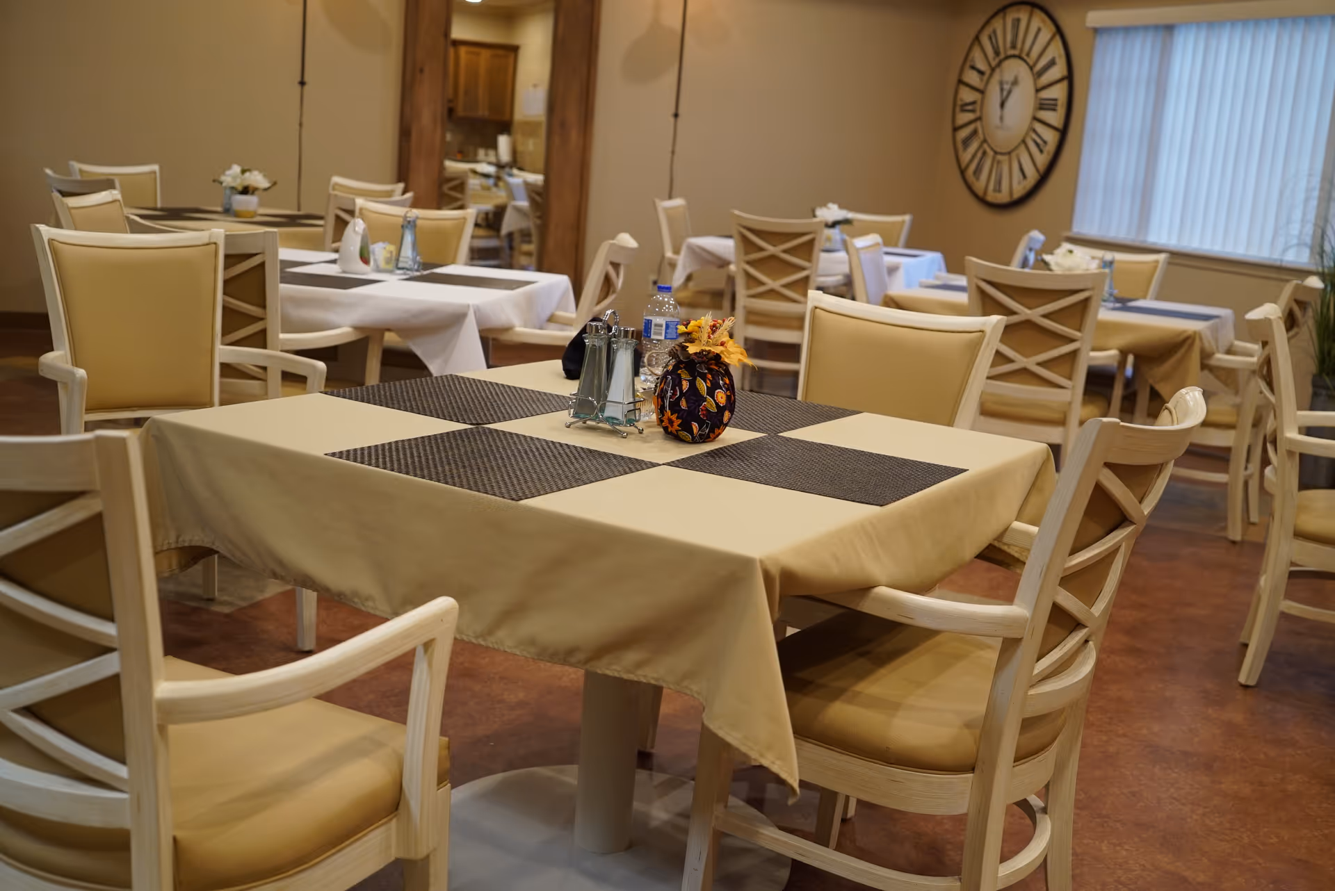 A dining room with square tables, beige chairs, and simple centerpieces.