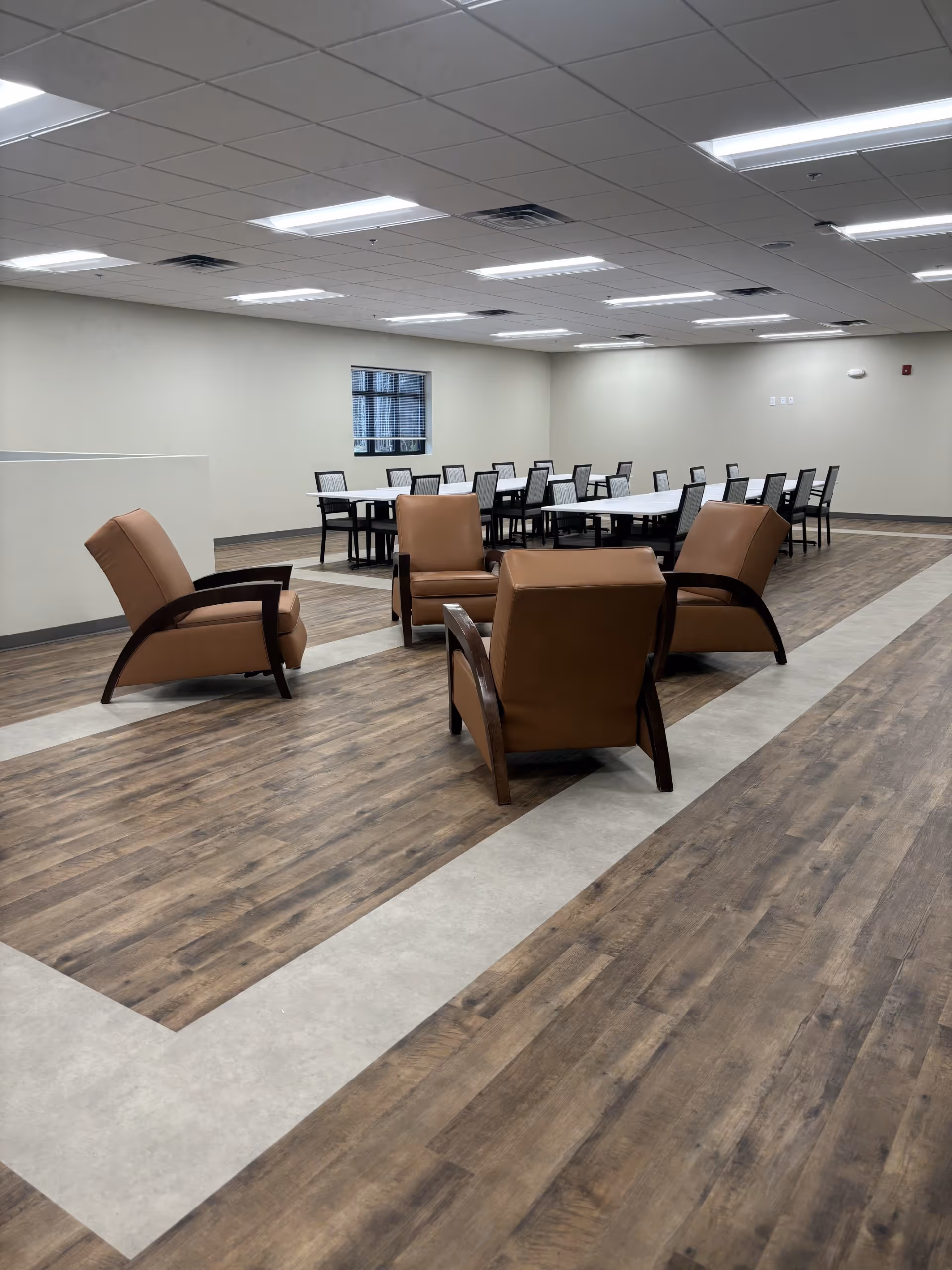 Lounge seating area with brown chairs; dining tables visible in the back of the room.