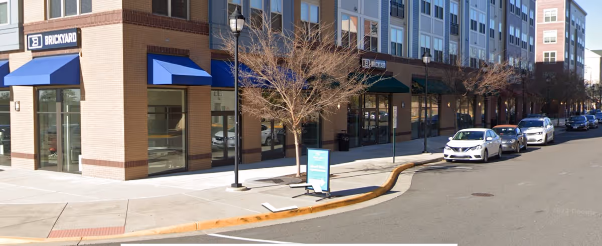 Exterior view of a multi-story brick building with blue awnings and parked cars along the street.