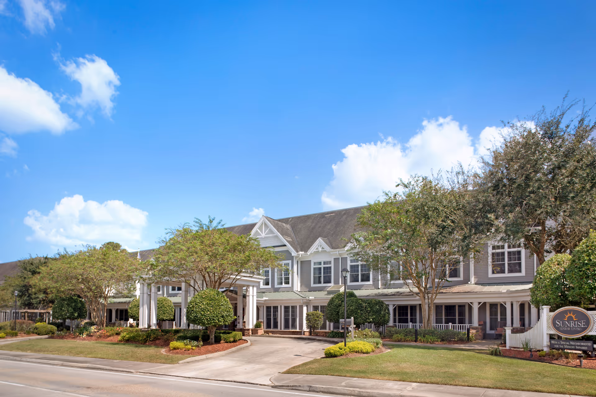 Sunrise at Siegen senior living exterior with manicured lawn and a bright blue sky.