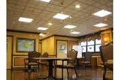 Warm, empty dining room with round tables and chairs in a senior living facility.