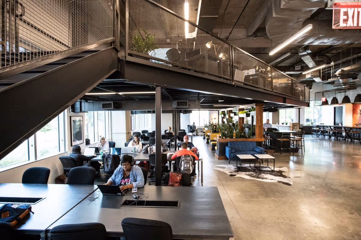 Open industrial-style communal lounge with tables, chairs, and residents working on laptops