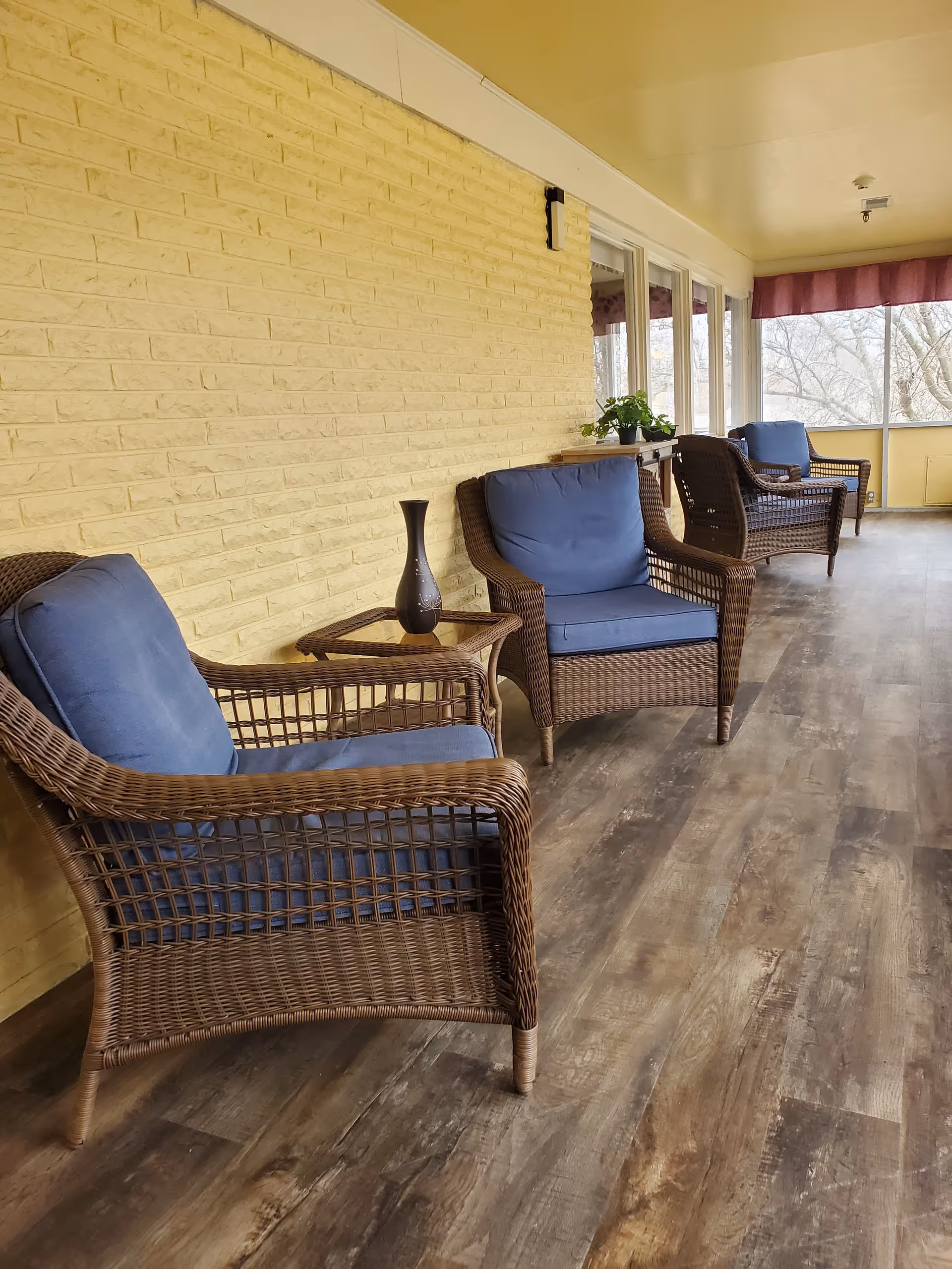 Covered outdoor seating veranda with wicker chairs and blue cushions along a brick wall.