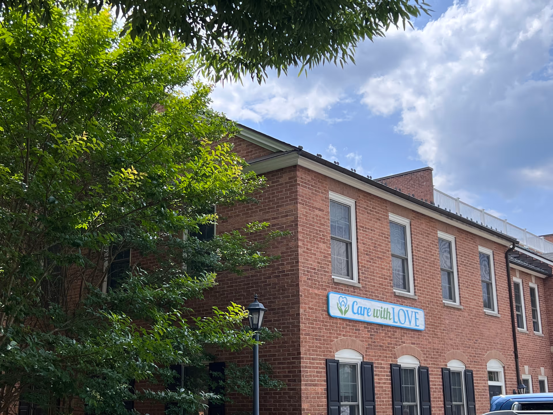 Brick senior living facility exterior with a 'Care with Love' sign on the facade.