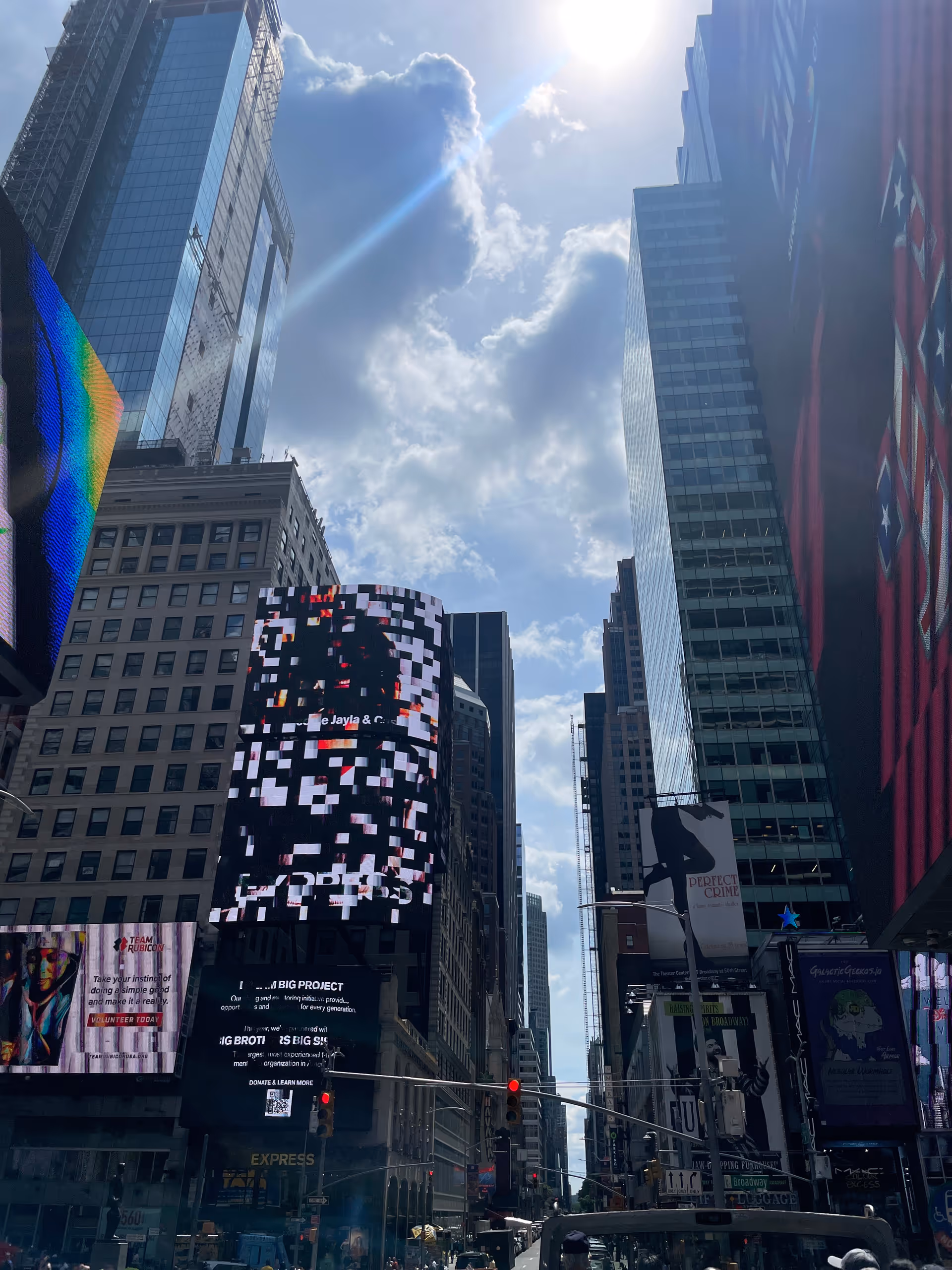 Tall glass skyscrapers flank a busy city street with oversized digital billboards.