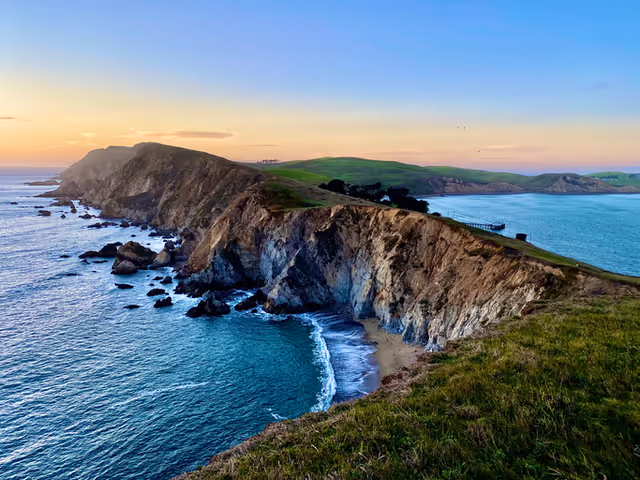 Sunset over rugged coastal cliffs, green fields, and blue ocean along the shoreline.