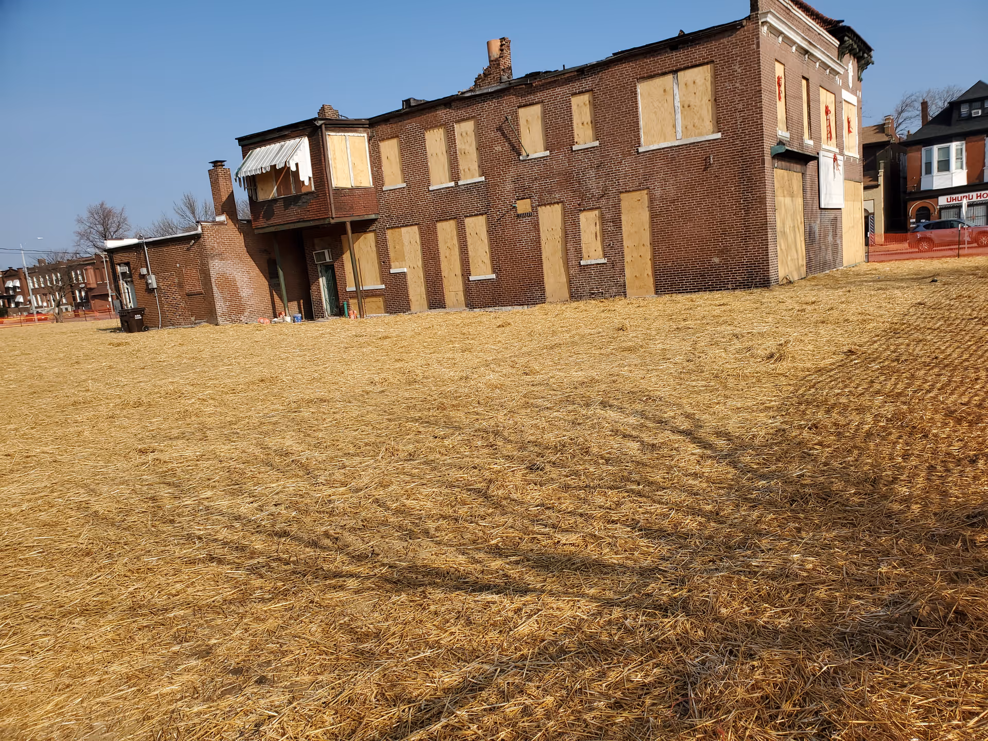 Boarded-up brick building with plywood windows on a dry, vacant lot.