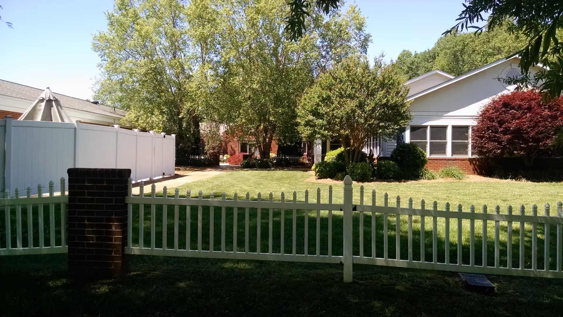 White picket fence borders a grassy yard with a single-story building and trees.