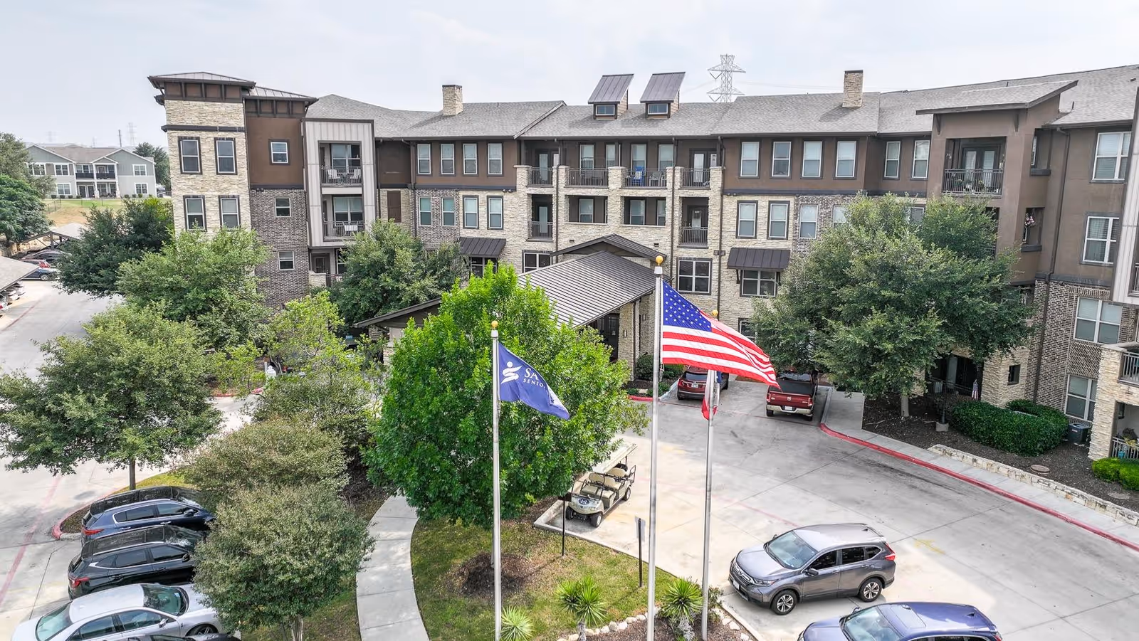 Exterior view of Landon Ridge Alamo Ranch senior living facility with flags and trees.