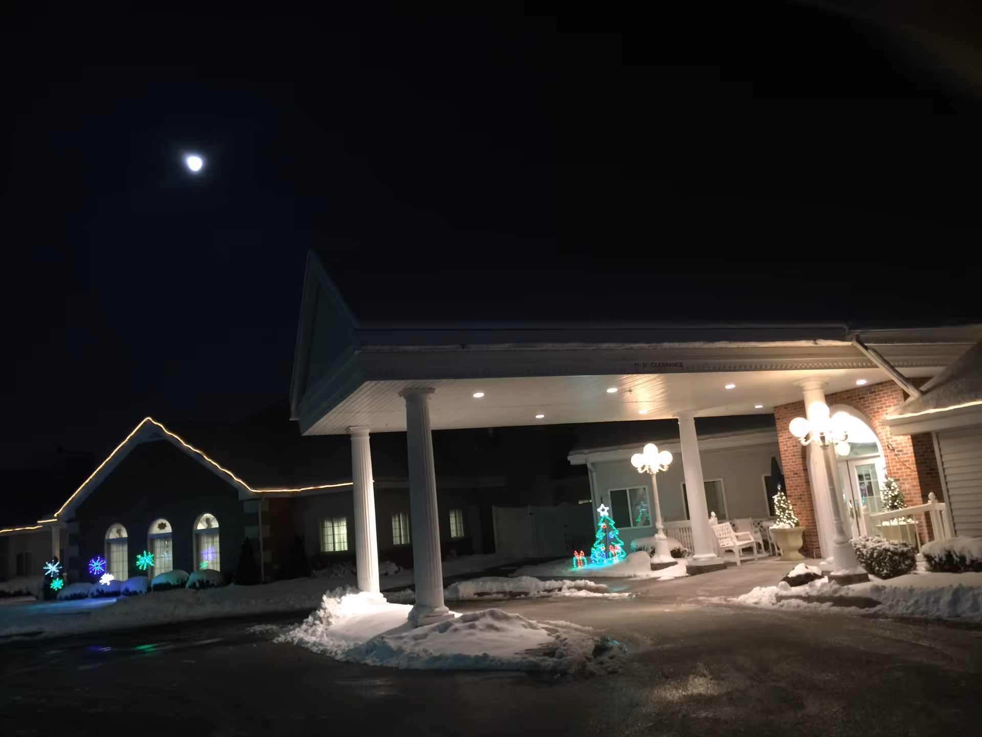 Night view of Hillcrest Health & Living entrance with snow and festive holiday lights.
