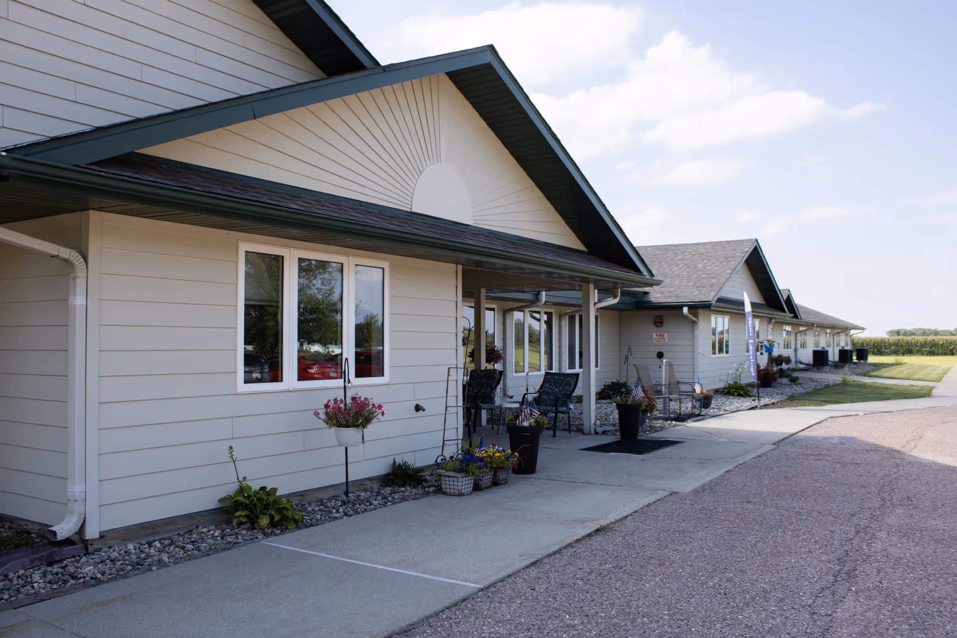 Row of beige senior living cottages with porches, planters, and a paved walkway.