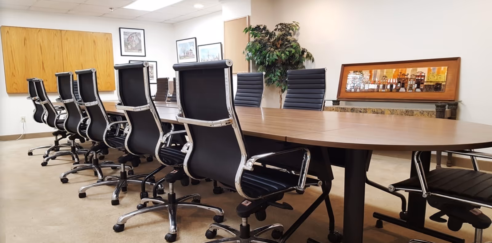 A long wooden conference table with black rolling chairs in a bright, corporate meeting room.