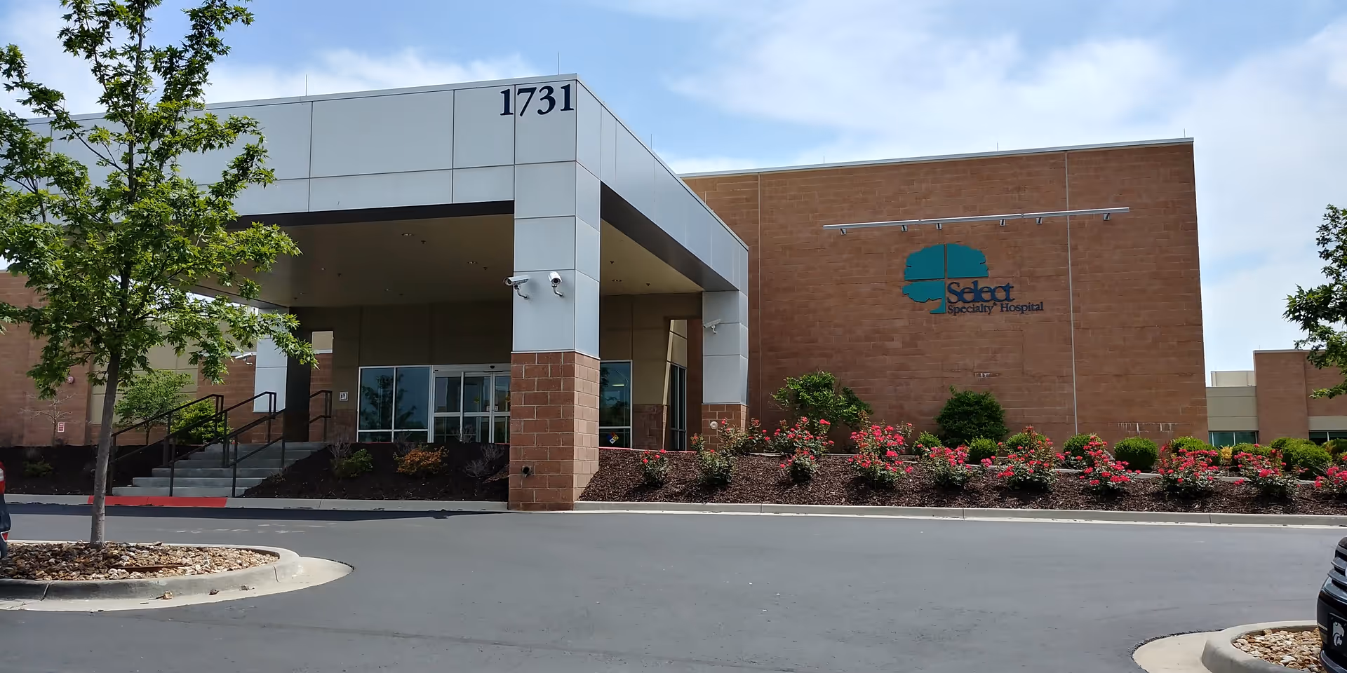 Modern medical facility exterior featuring the entrance, landscaped shrubs, and a Select Specialty Hospital sign.