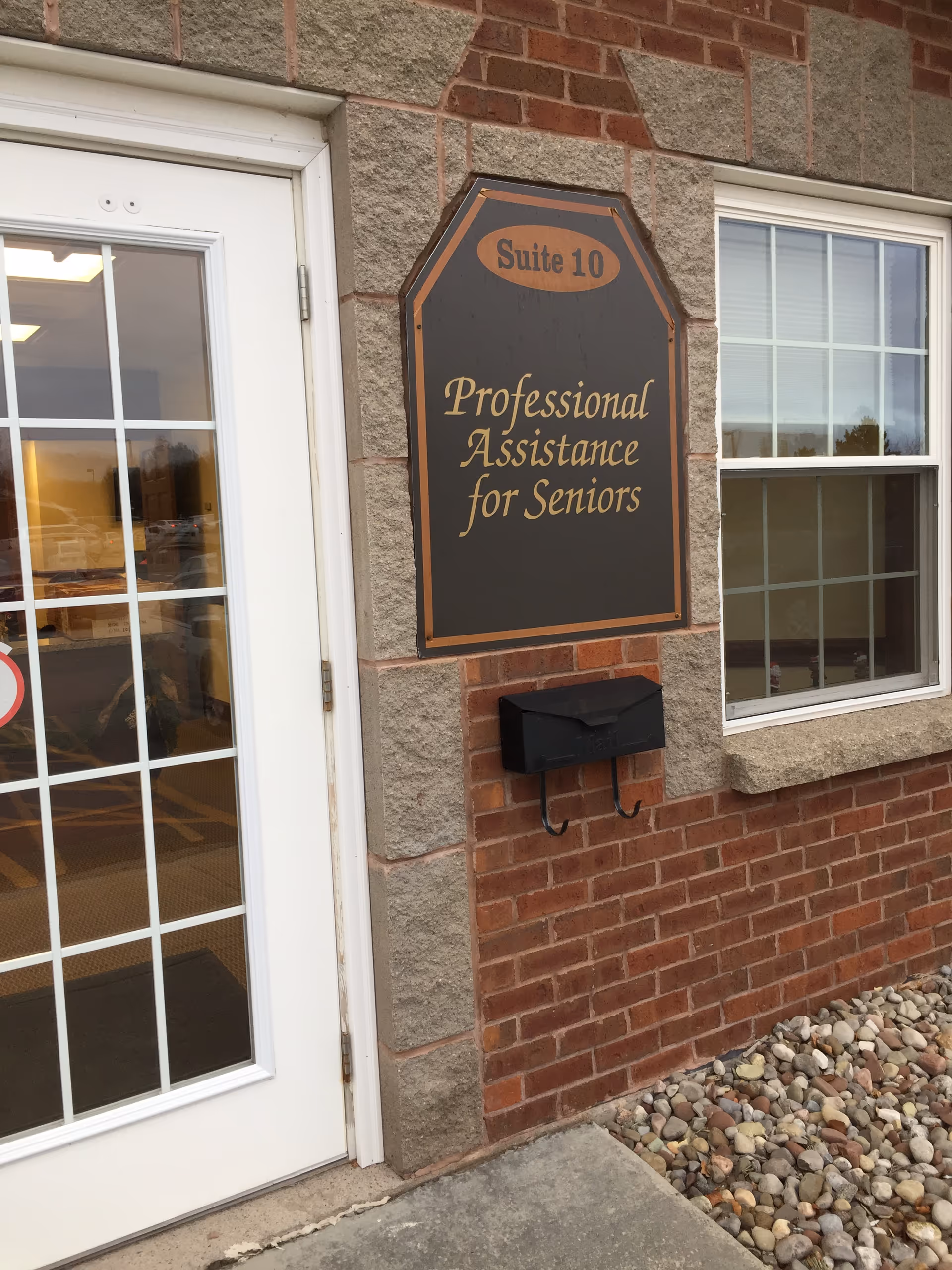 Brick exterior with a sign 'Professional Assistance for Seniors' beside a glass door.