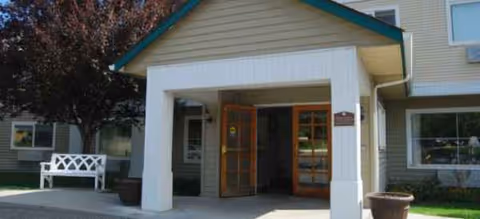 Exterior view of Brookdale Meadow Springs entrance with double wooden doors and a bench