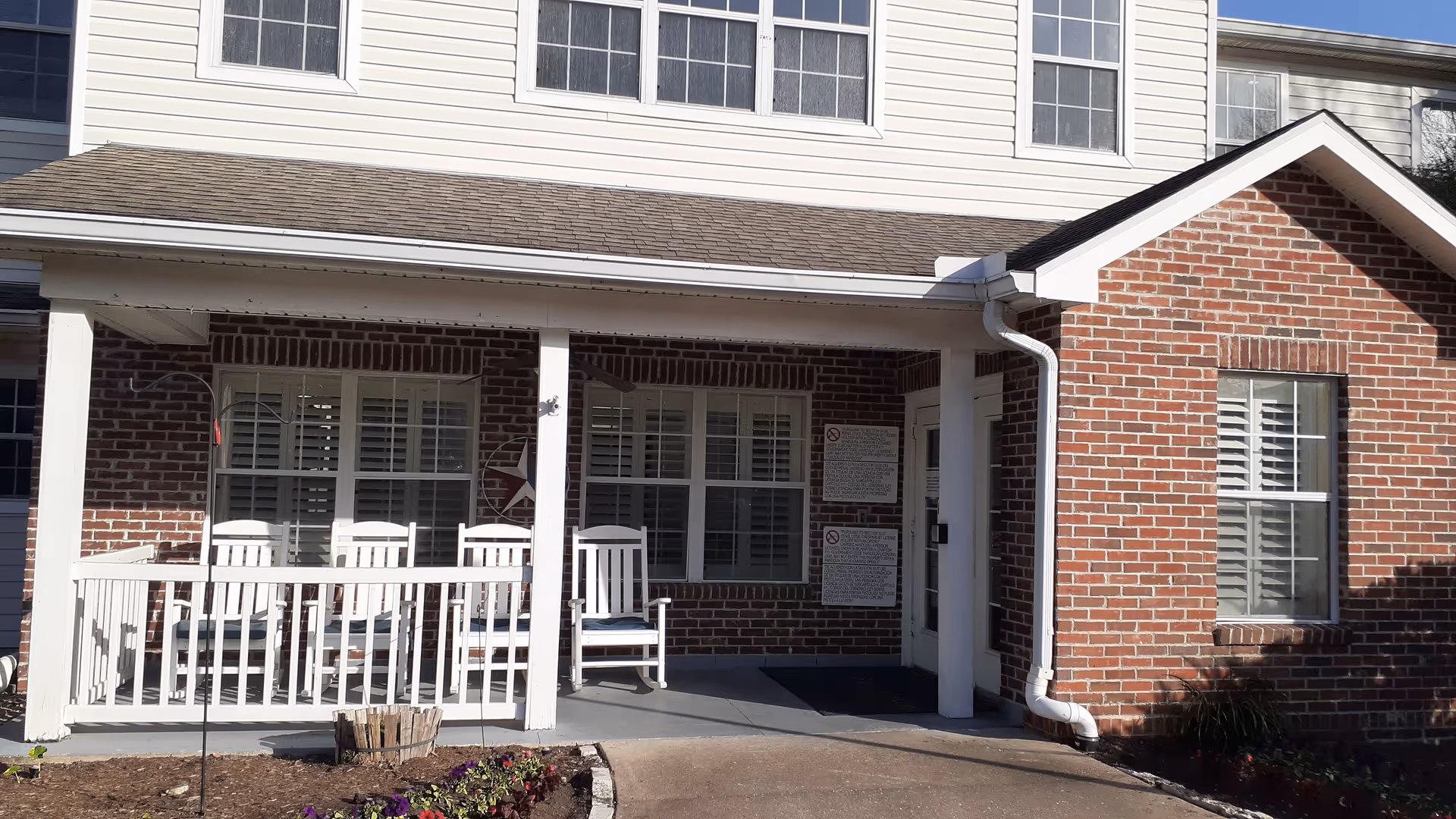Front entrance of Brookdale the Heights with a brick exterior and white rocking chairs.