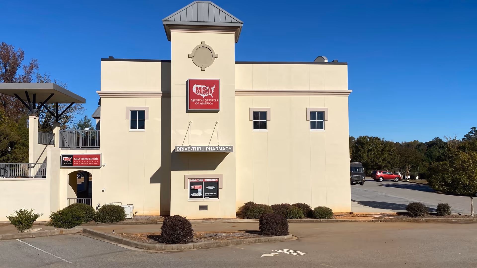 Beige medical building with drive-thru pharmacy sign and parking lot under blue sky.