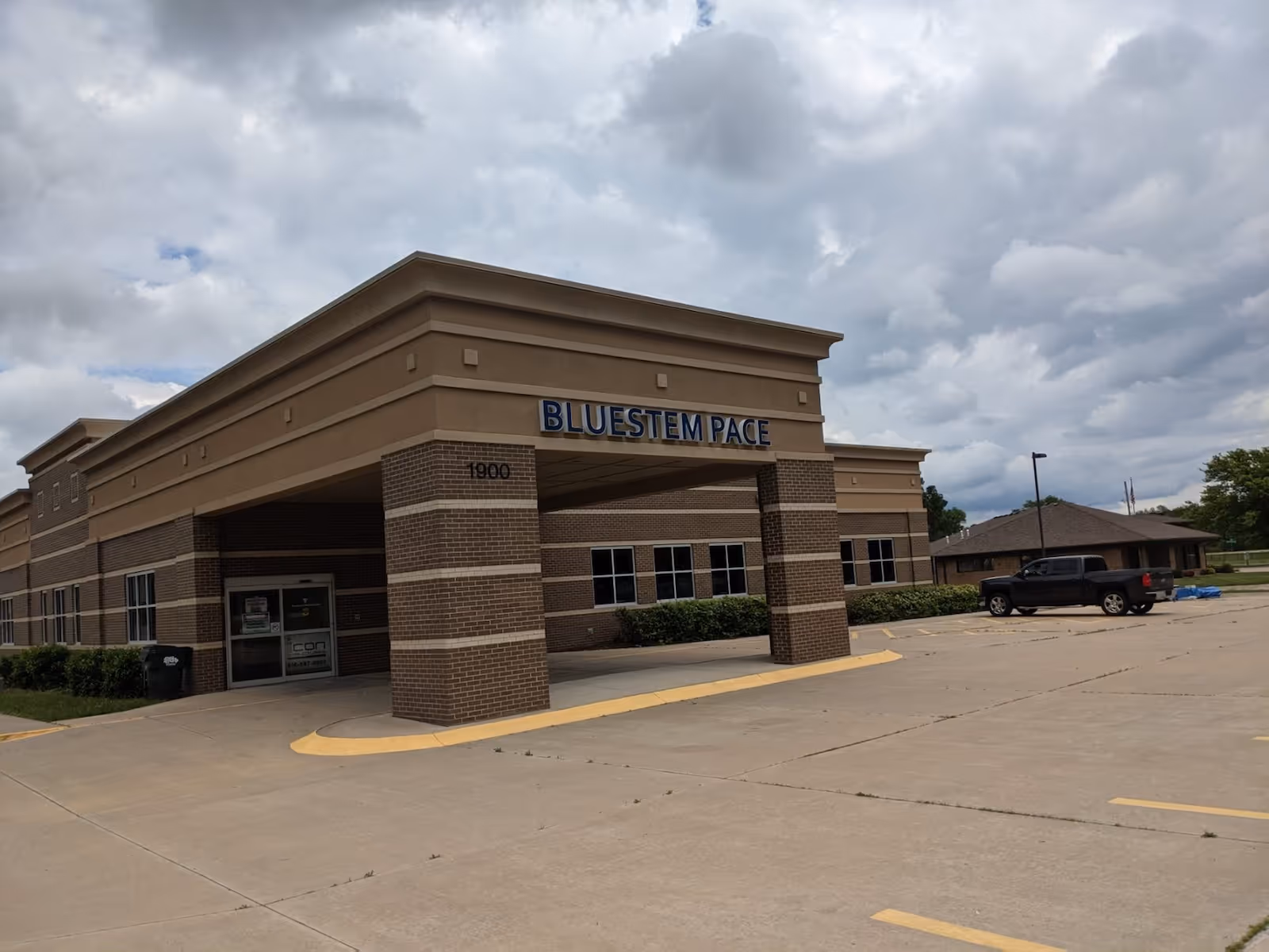 Exterior view of Bluestem PACE facility with parking lot and cloudy sky.