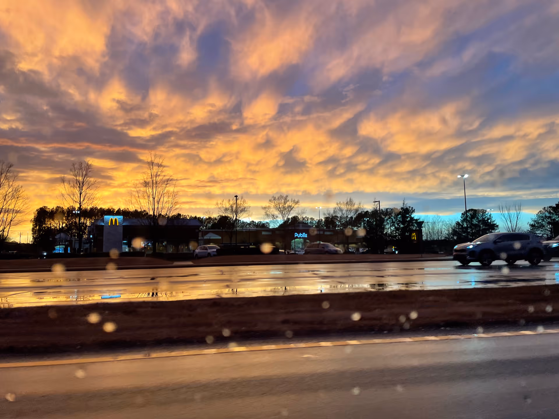 Sunset sky over a strip mall, with McDonald's and Publix across a wet road.