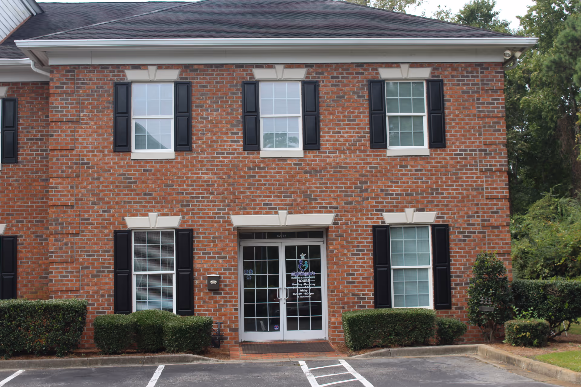 Brick two-story facility with large front entrance and black shutters, parking lot in foreground.