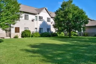 Front exterior of a Galeon senior living building with green lawn and trees.