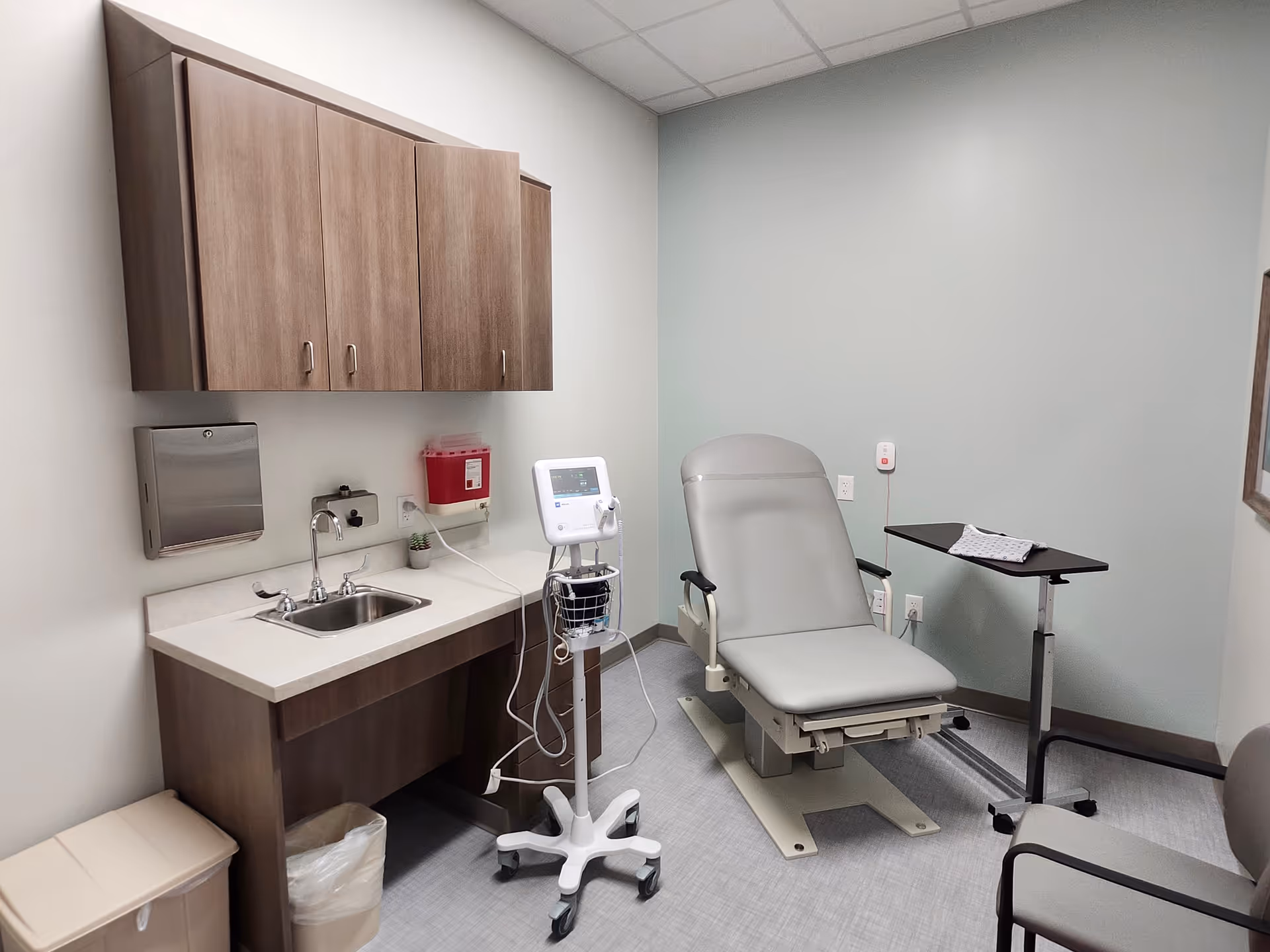 A medical examination room with a reclining chair, sink, cabinets, and medical equipment.