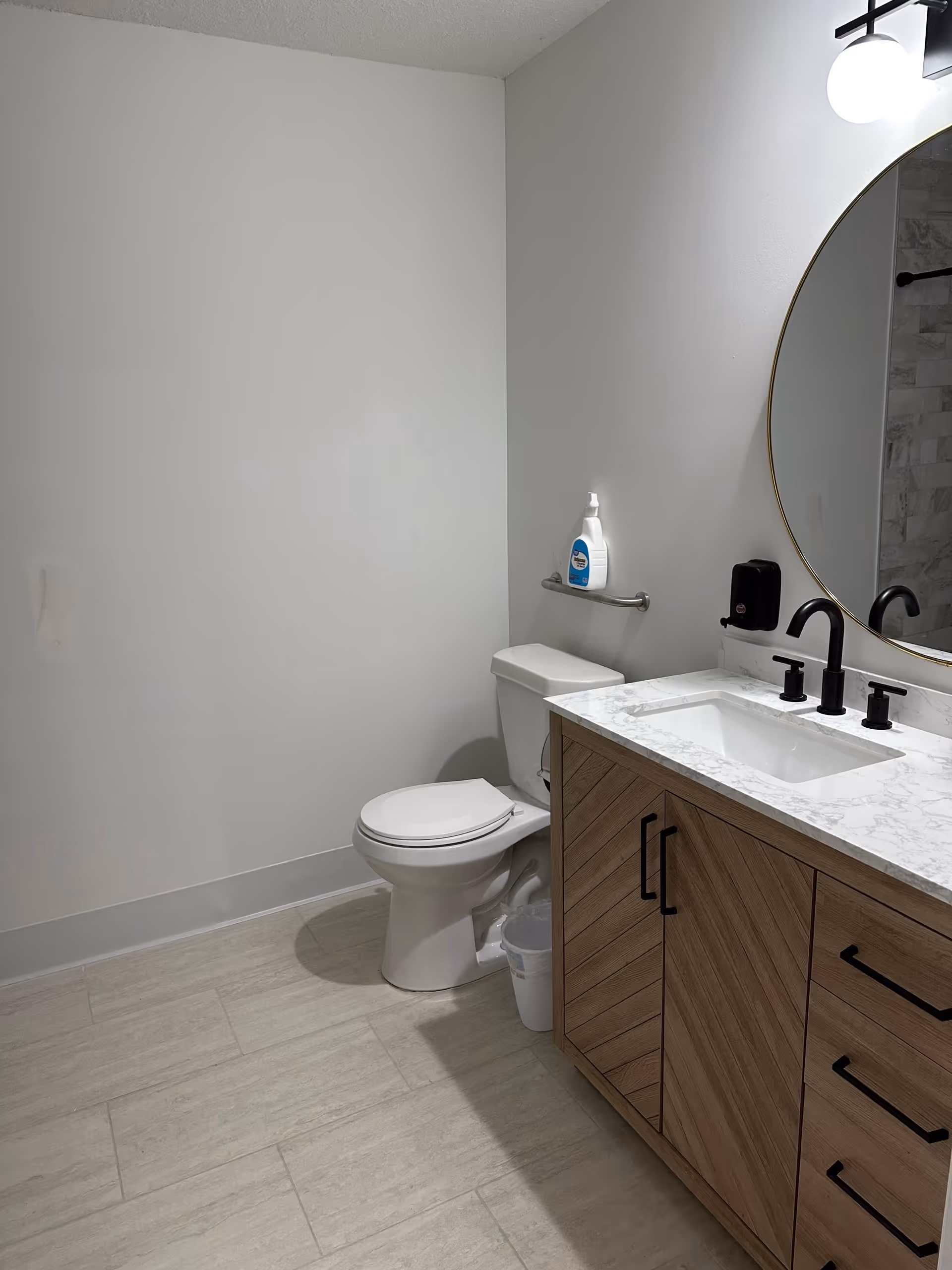 Modern bathroom with toilet, sink, round mirror, and marble countertop.