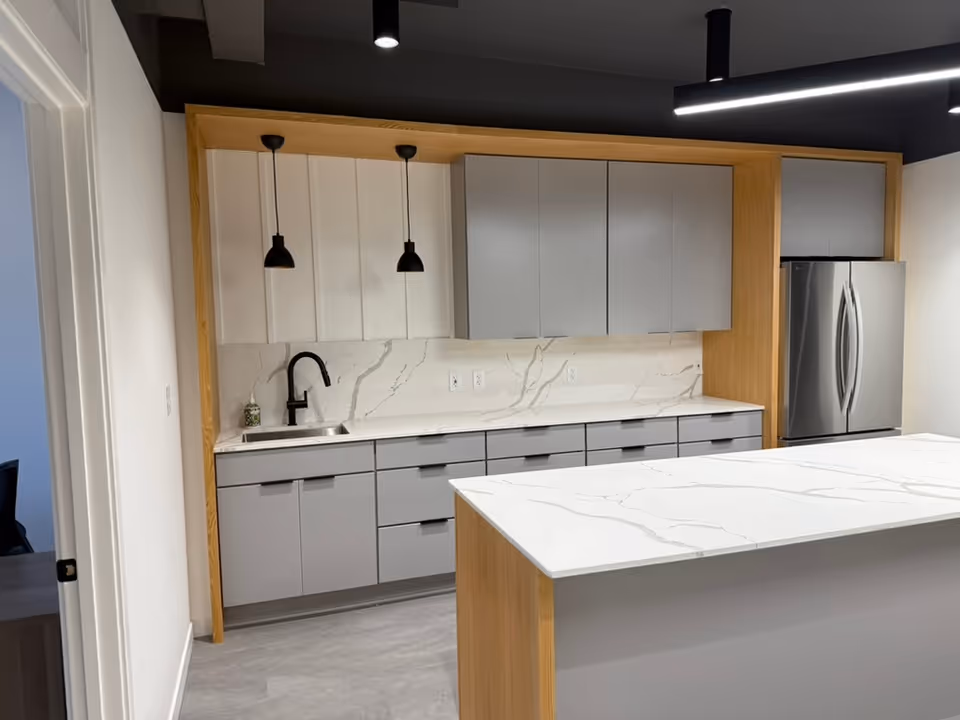 Modern kitchen with gray cabinets, marble countertops, island, sink, and stainless steel refrigerator.