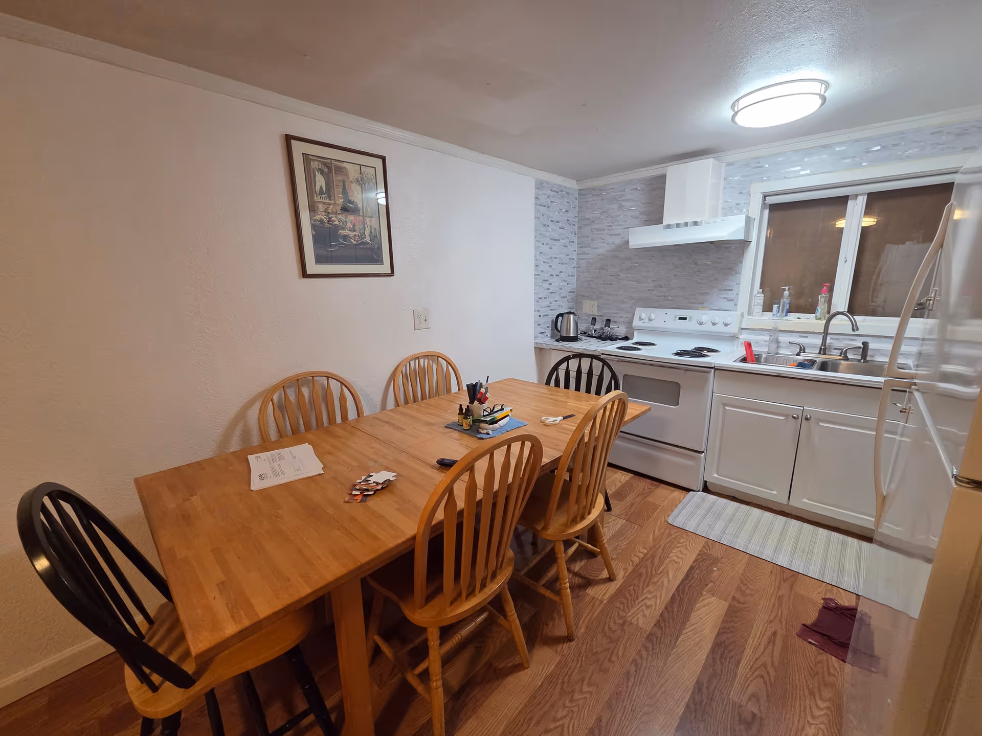 Wood dining table with six chairs adjacent to a compact kitchen.
