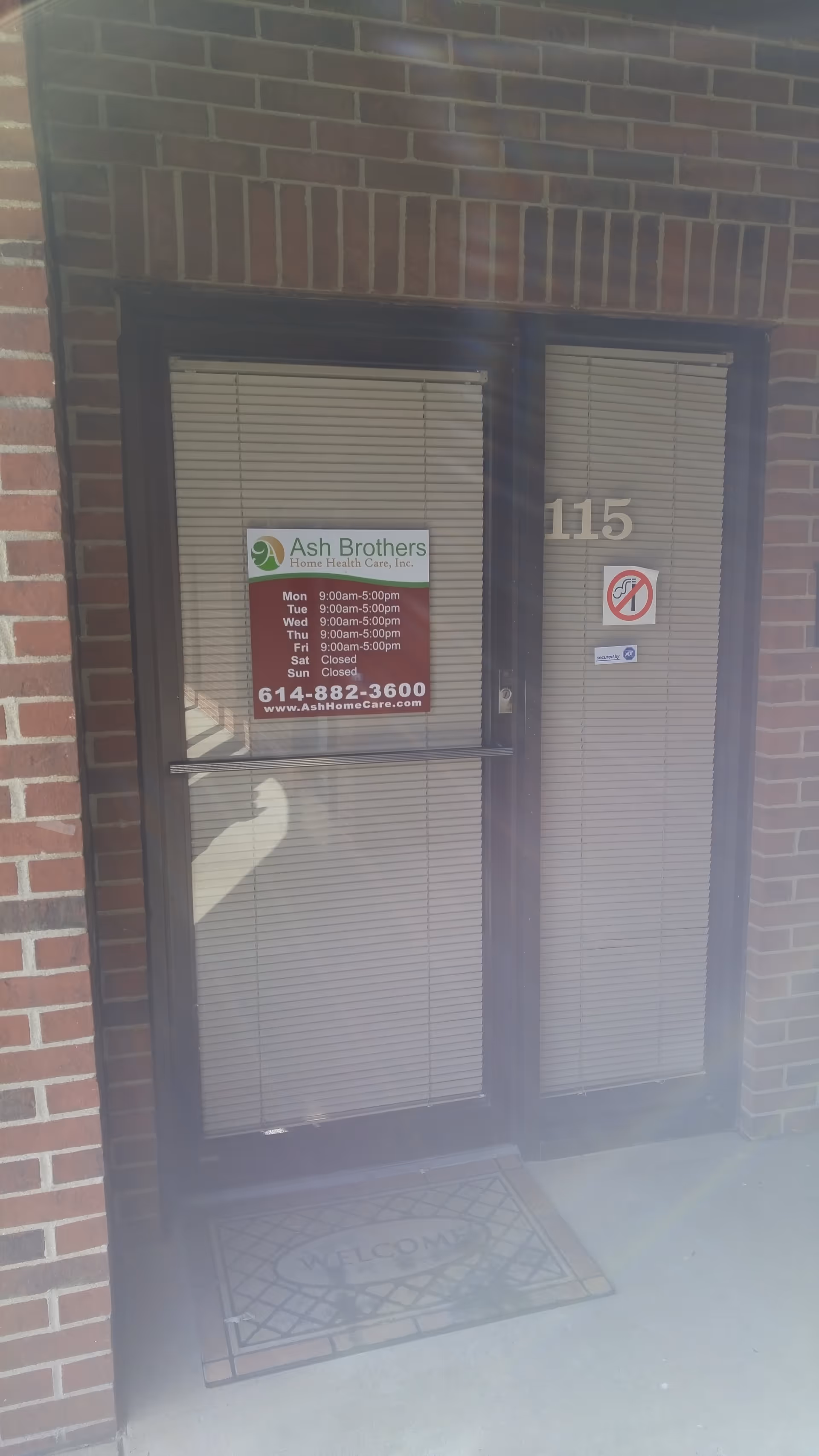 Brick building entrance with door, blinds, 115, and sign for Ash Brothers Home Health Care.