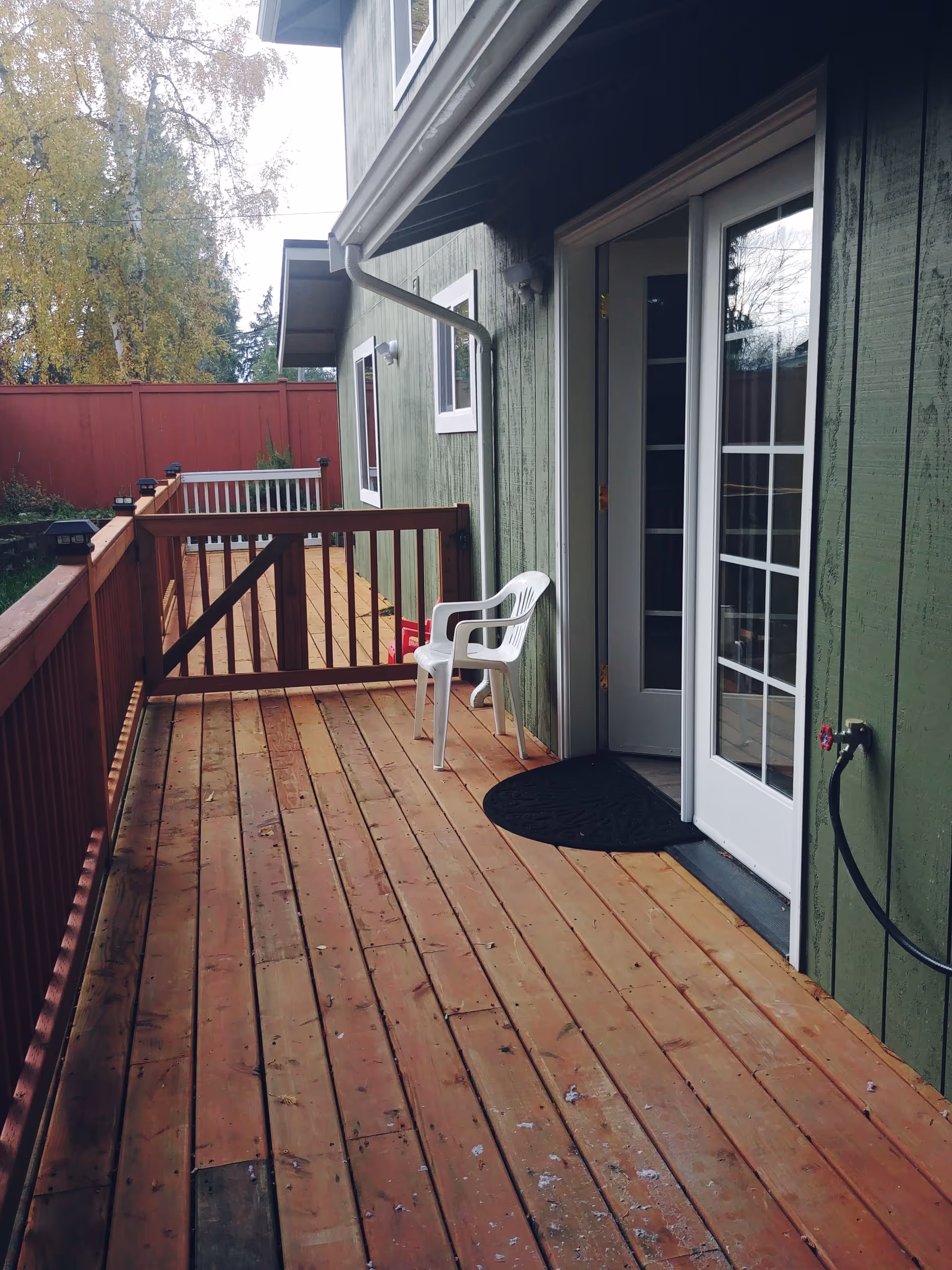 A wooden deck with a white plastic chair beside a green exterior door.