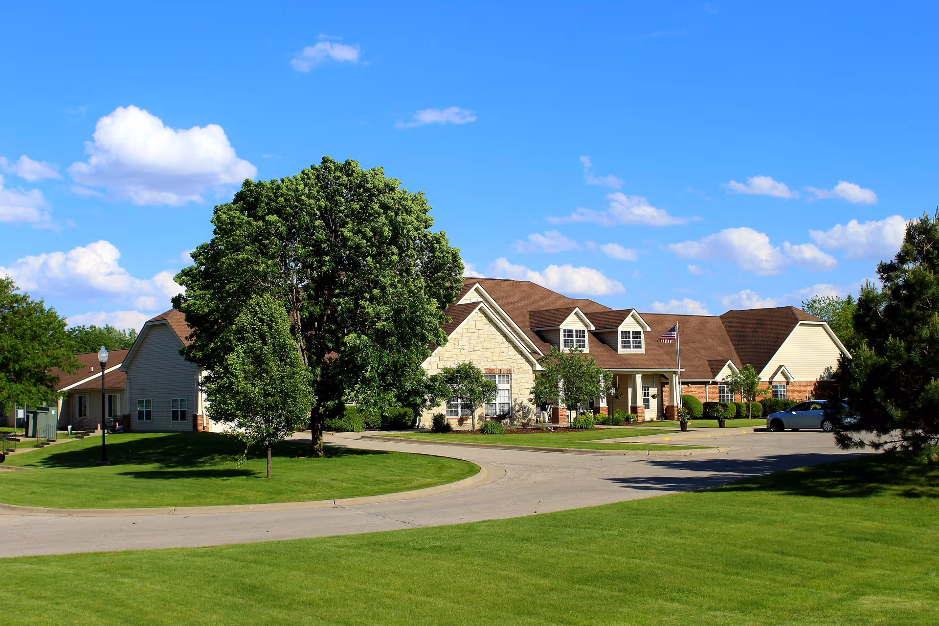 Front exterior of Bickford of Marshalltown, senior living facility with a large tree and manicured lawn.