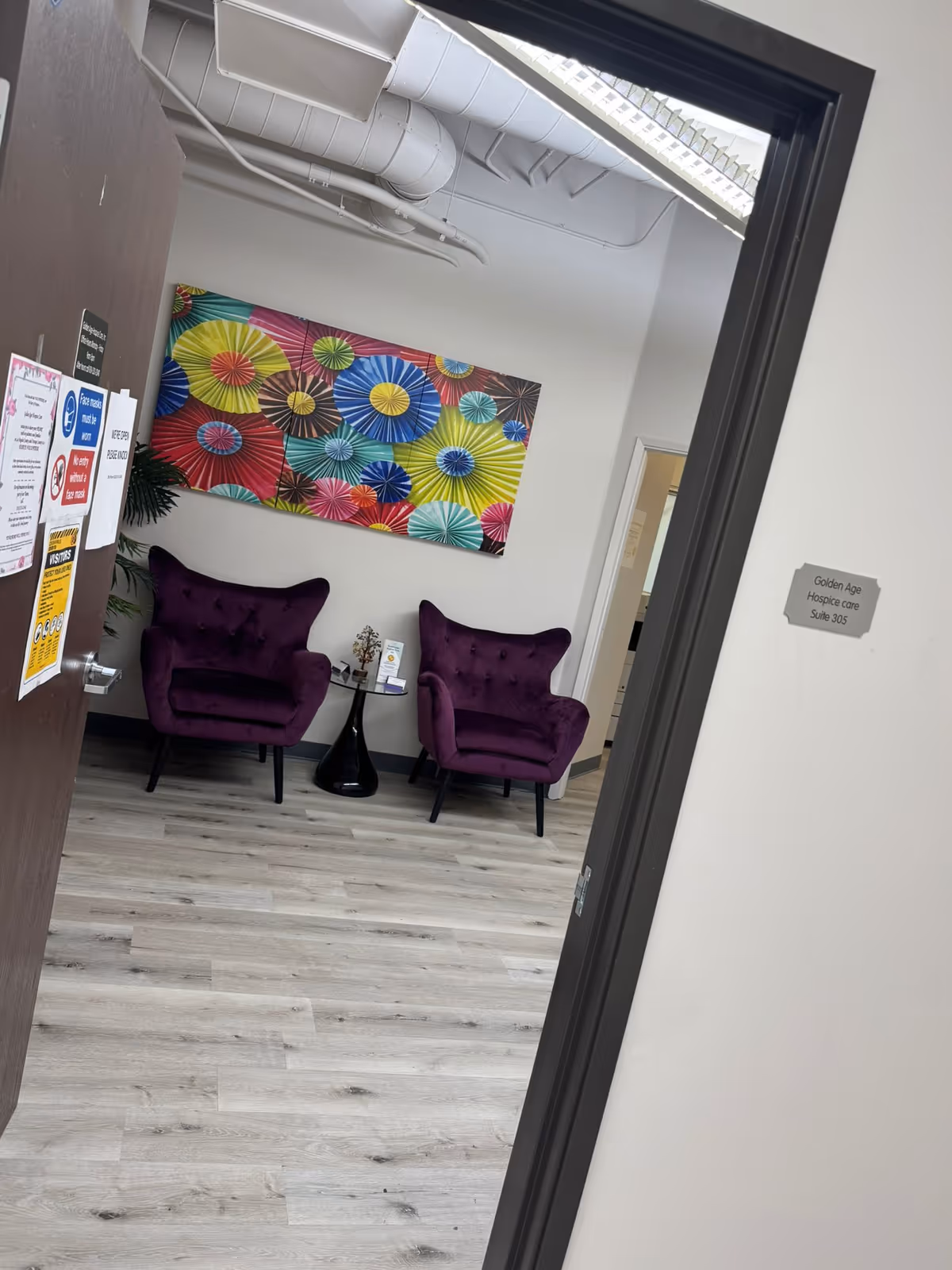 Two purple chairs flank a table in an indoor waiting area with colorful wall art.
