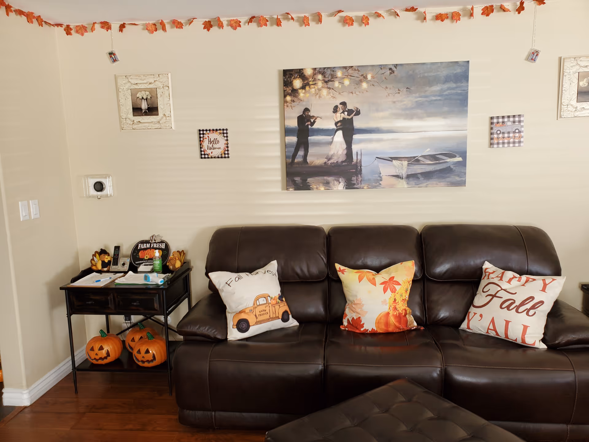 Cozy living room with a brown leather sofa, fall pillows, and wall art.