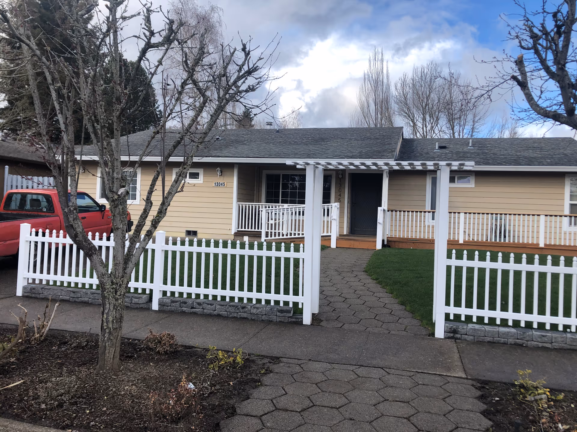 Single-story beige care home with white picket fence and a red truck in driveway.